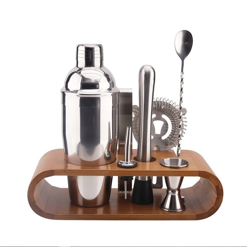Sept accessoires à cocktail en inox rangés sur leur support en bambou