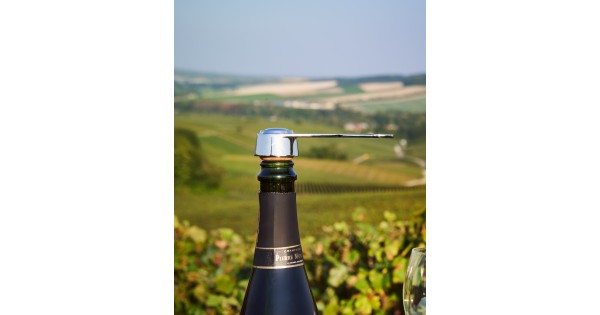 Pince L’Atelier du Vin posée sur le bouchon d’une bouteille devant les vignes